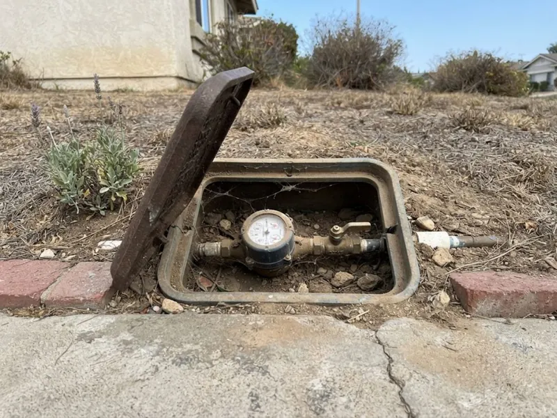 Open water meter box with meter and shutoff valve in front of a Mission Viejo home